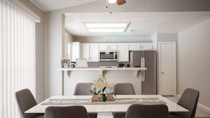 Una cocina moderna con armarios blancos, un microondas y un refrigerador. Hay una mesa de comedor con cuatro sillas y un jarrón con flores.