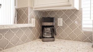 Una cafetera sobre una encimera de cocina con un salpicadero decorado y armarios blancos.