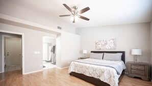 Un dormitorio con cama, mesitas de noche, ventilador de techo y un cuadro en la pared.