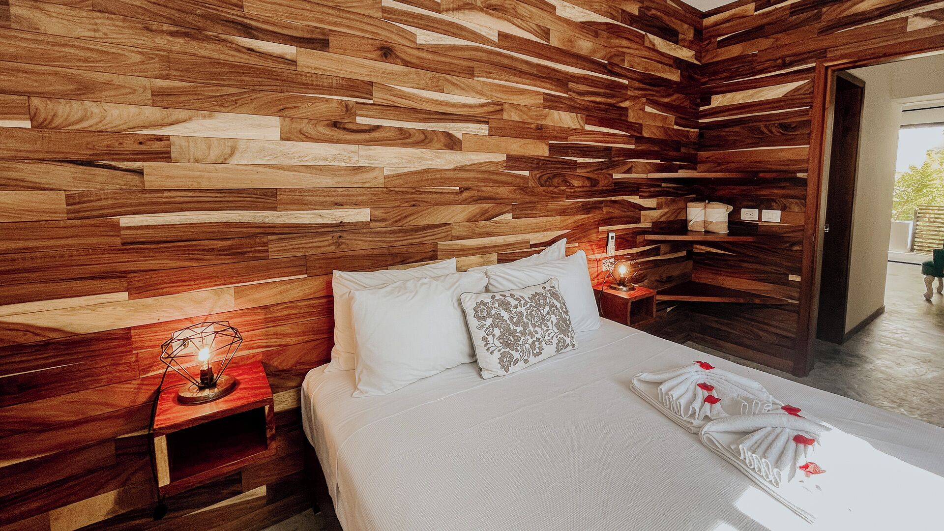 A bedroom with a wooden slat wall design, a bed with white linens, and a nightstand with a lamp.