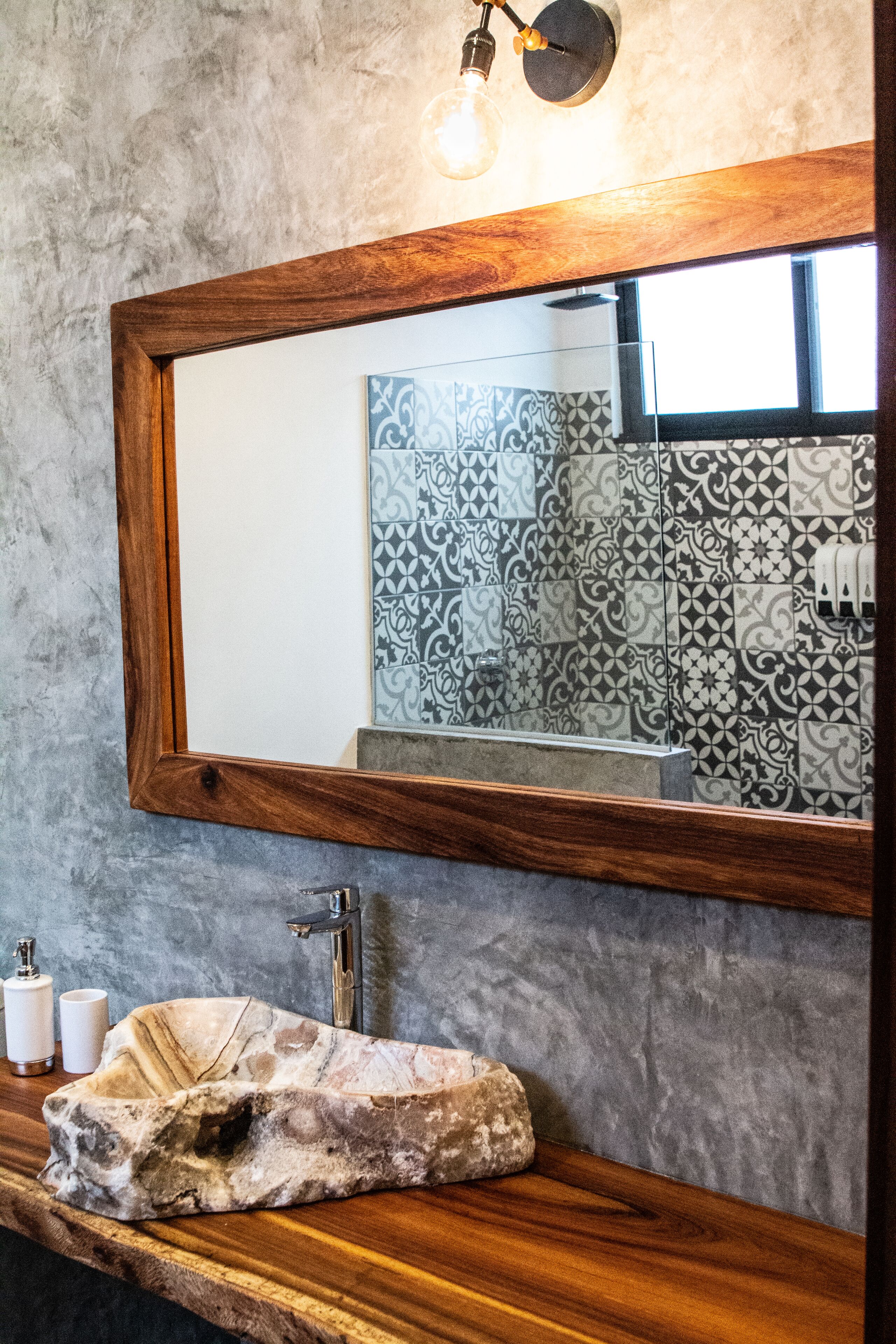 Un baño con espejo de marco de madera, lavamanos de mármol y baldosas estampadas.