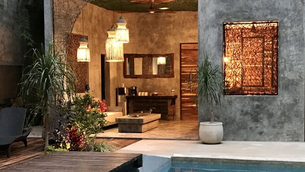 A modern indoor pool area with a wooden deck, lounge seating, and a large potted plant. - Little Gem Hotel Tulum La Veleta (Tulum)