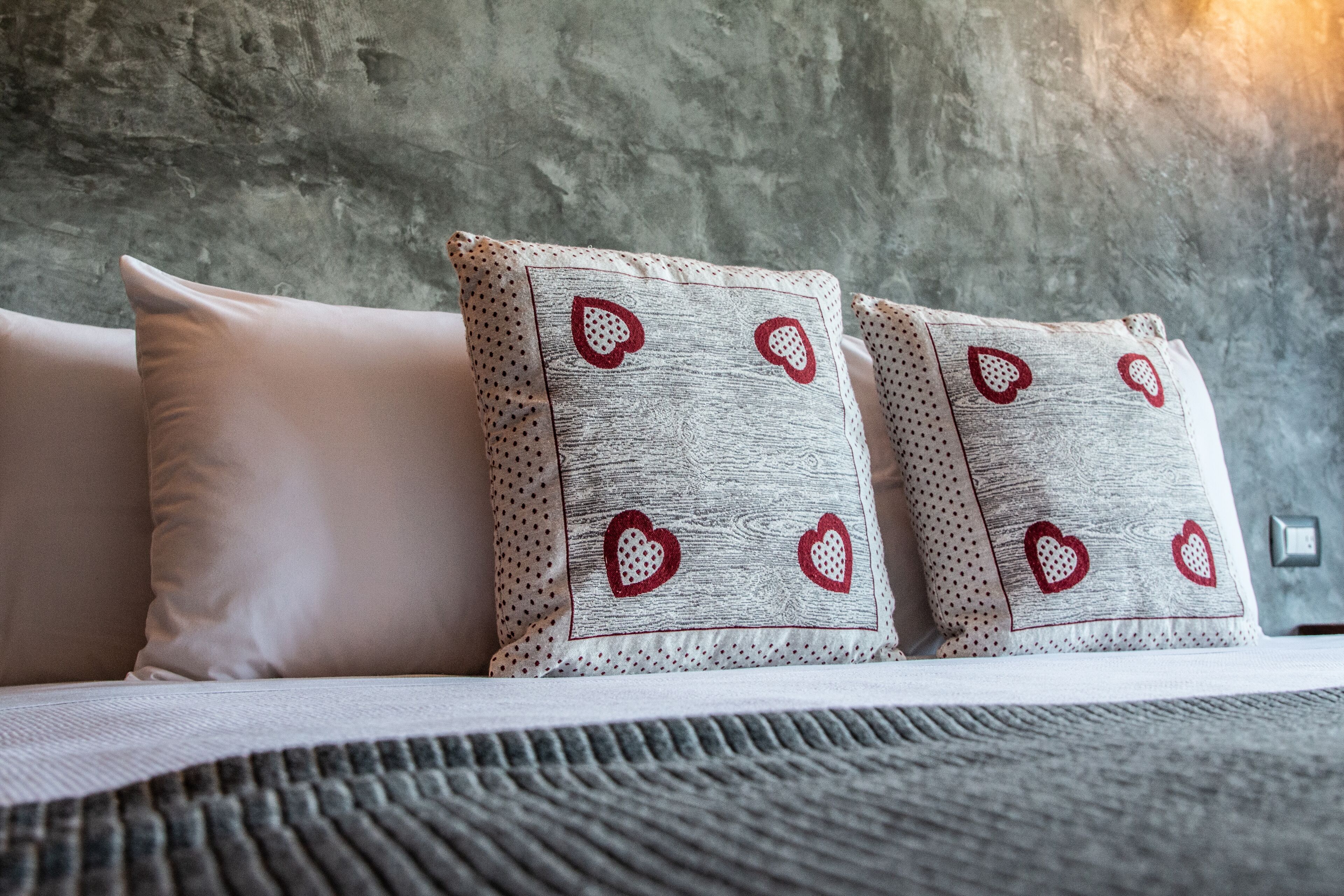 A bed with three pillows, two with heart patterns and one plain.