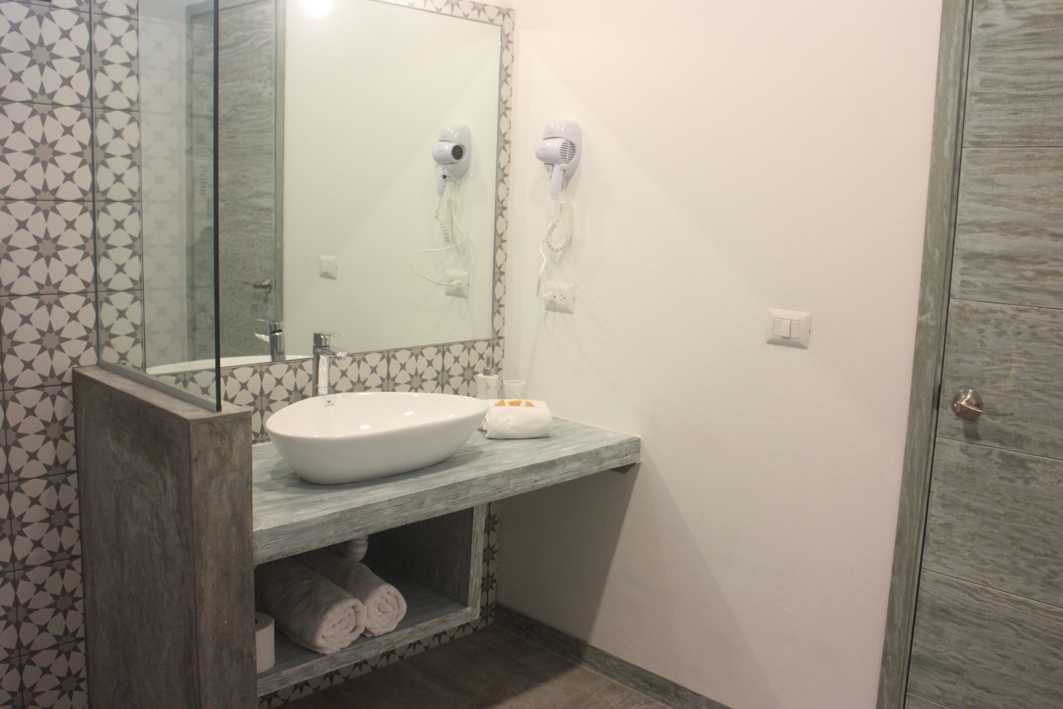 Une salle de bain avec un lavabo blanc, un miroir et deux sèche-cheveux fixés au mur.