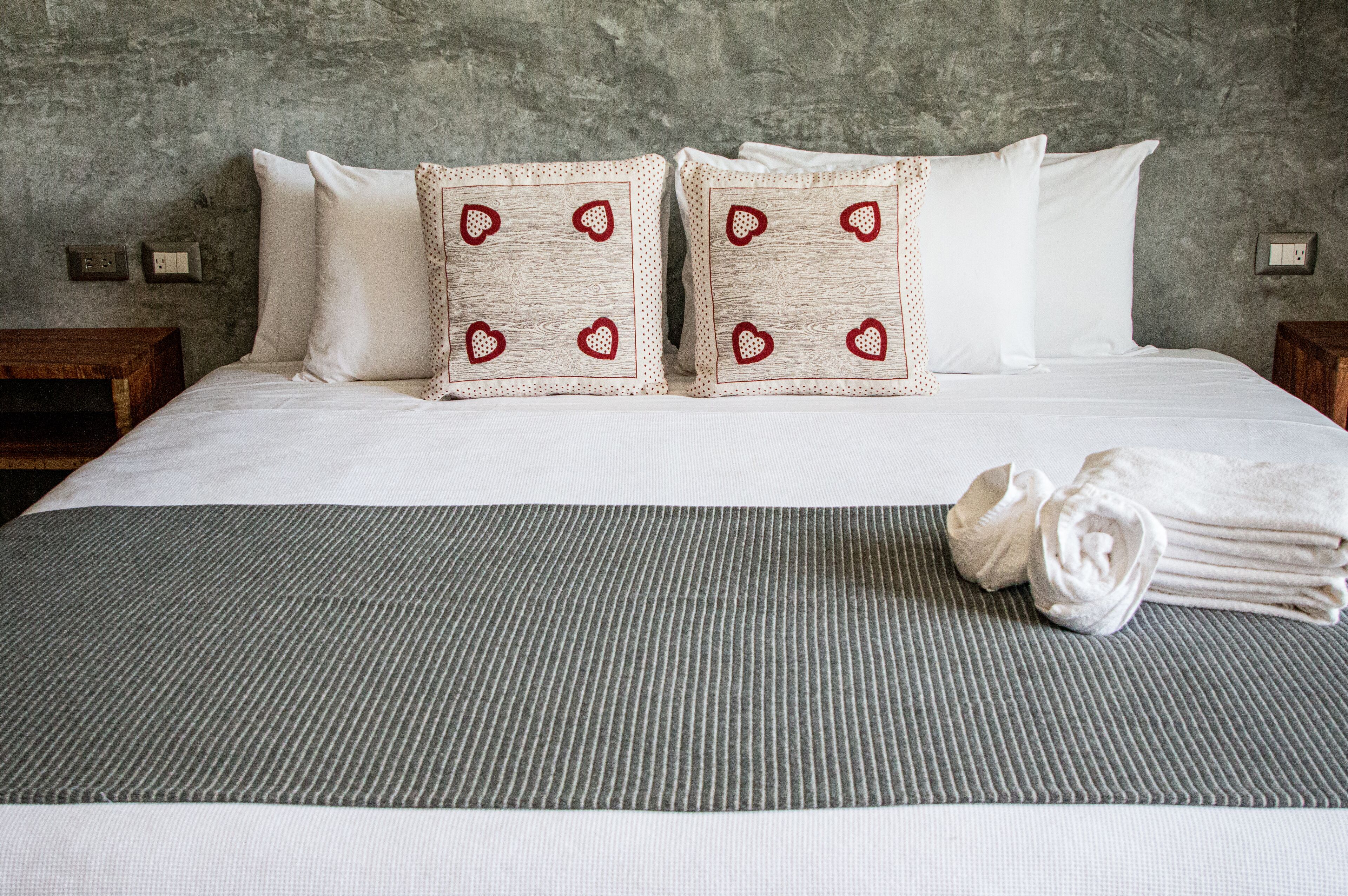 A neatly made bed with a striped bedspread, two pillows with heart patterns, and a rolled towel on the bed.