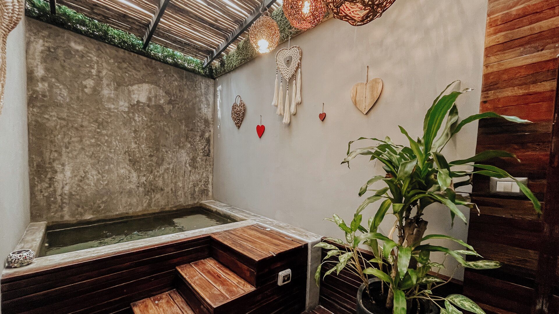 Un cuarto de spa con un banco de madera, un jacuzzi pequeño y adornos colgantes en la pared.