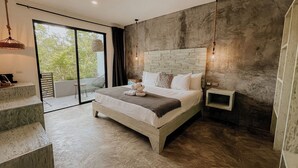 A modern bedroom with a stone headboard, a large bed, a bedside table, and a view of greenery through a sliding door. - Little Gem Hotel Tulum La Veleta (Tulum)