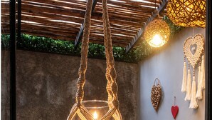 A room with a hanging macrame light fixture, a wooden bench, a wall-mounted heater, and a vase with red flowers. - Little Gem Hotel Tulum La Veleta (Tulum)