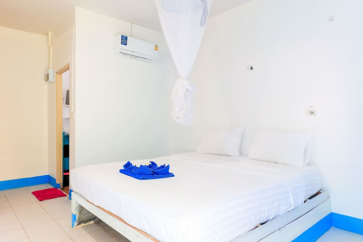 Une chambre à coucher avec un lit, du linge de lit blanc, un tapis rouge, un appareil de climatisation blanc et une moustiquaire blanche.
