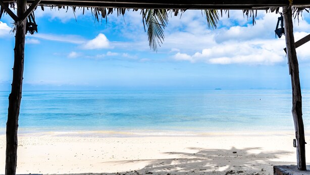 Blick auf einen Strand von einer Holzhütte mit einem Reetdach, mit Blick auf einen Sandstrand und ruhige See.