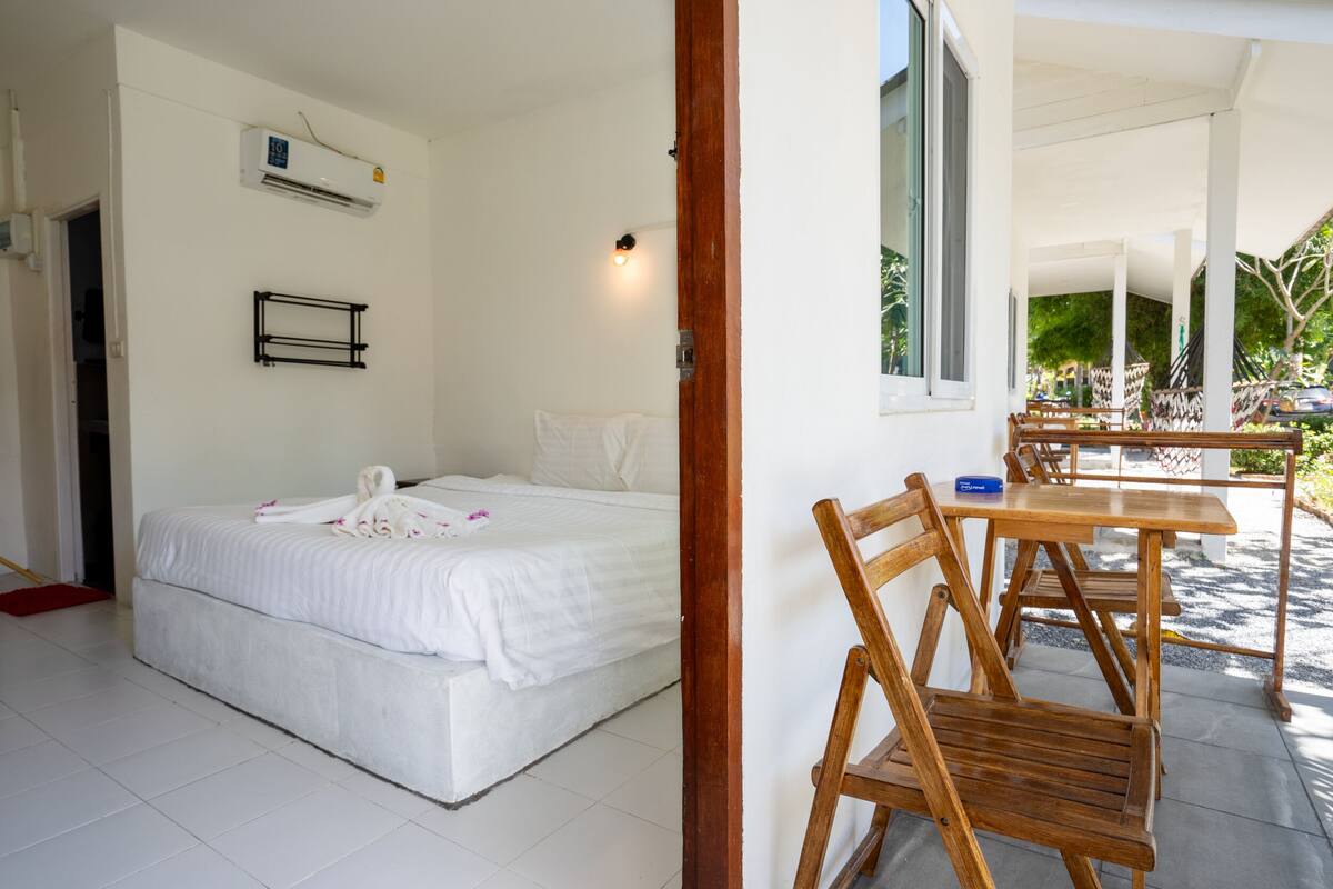 Une chambre d’hôtel avec un lit, une chaise en bois, une table et un appareil de climatisation.