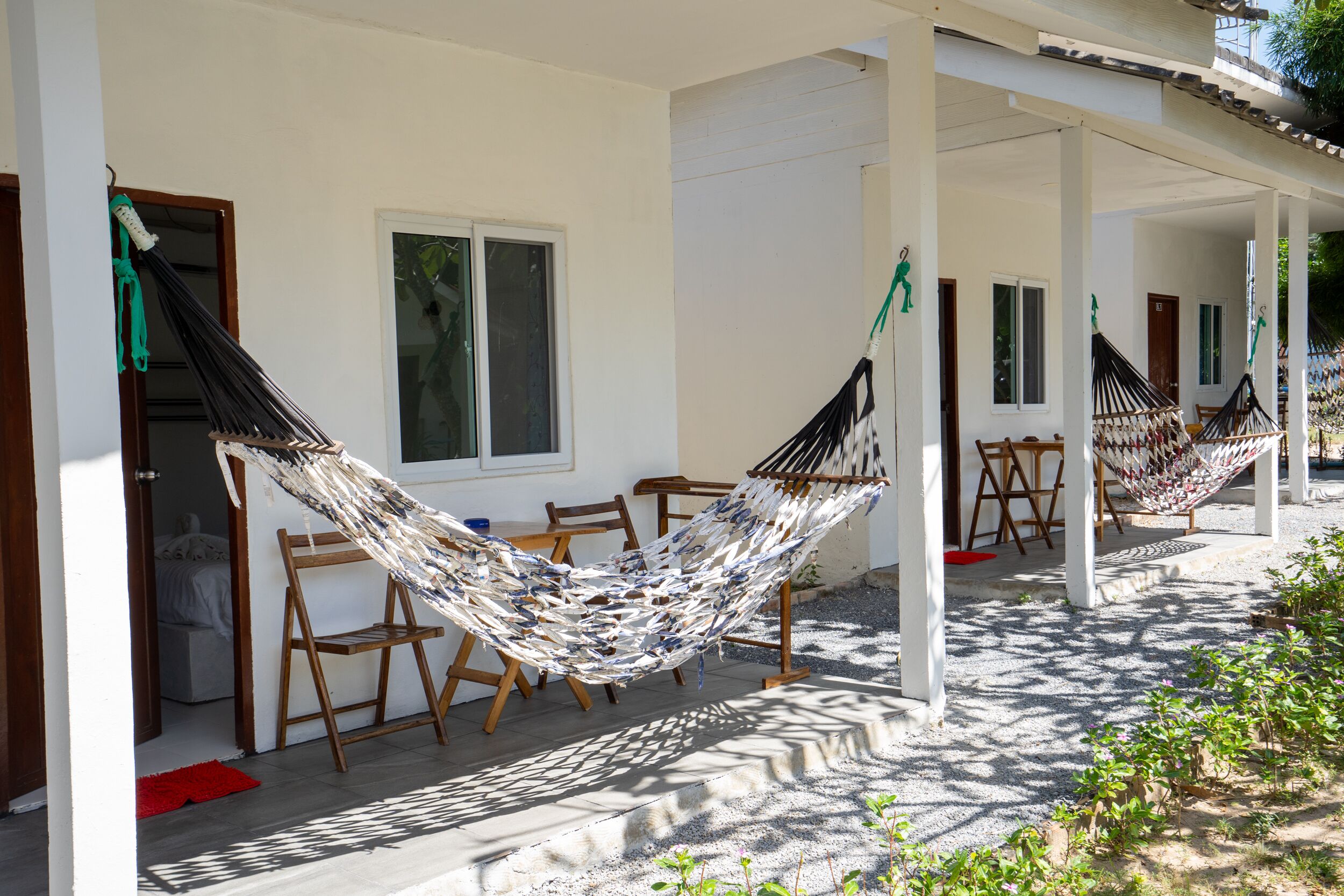 A hammock set up on a porch with a table and chairs, a window, and a door.