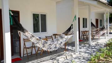 A hammock set up on a porch with a table and chairs, a window, and a door.