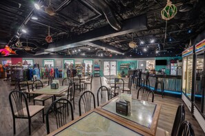 A restaurant with tables and chairs, a bar area, and a clothing store in the background. - Hilton Head Resort Condo with Private Beach Boardwalk & Indoor Pool! (Hilton Head Island)