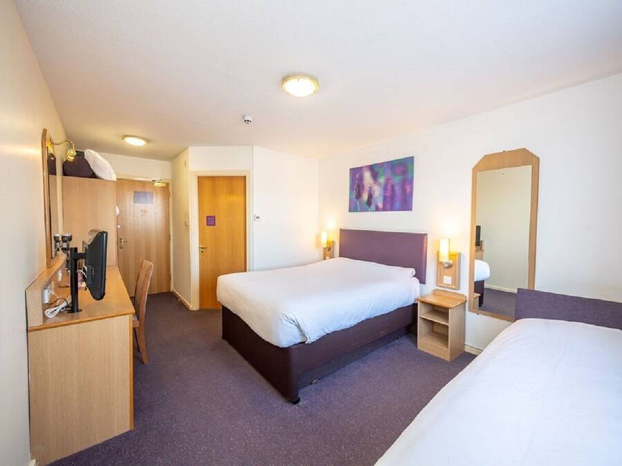 A hotel room with a single bed, a desk with a computer, a chair, a wardrobe, and a mirror.