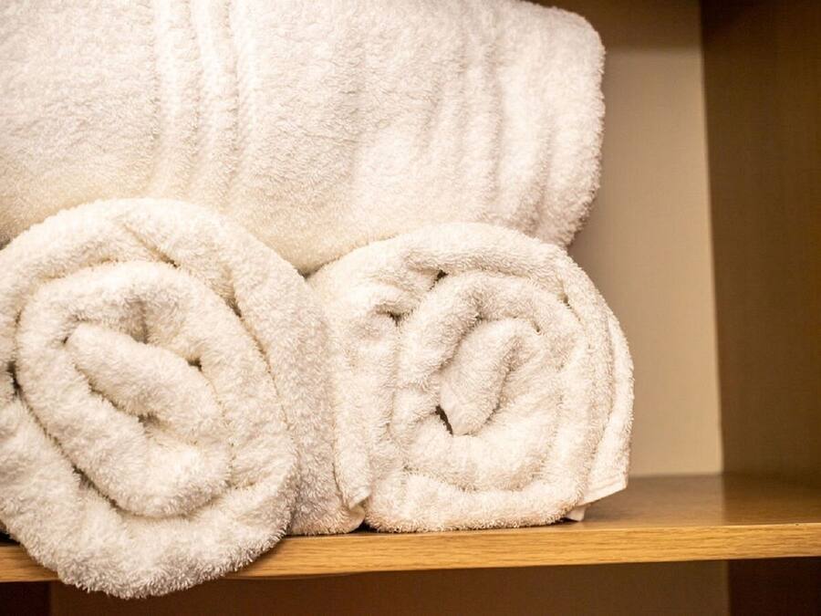 A wooden shelf with two rolled white towels.