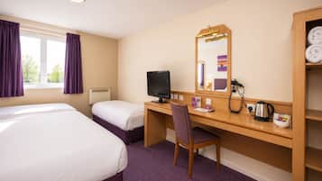 A hotel room with two beds, a desk with a computer, a chair, a mirror, a heater, and a shelf with towels.
