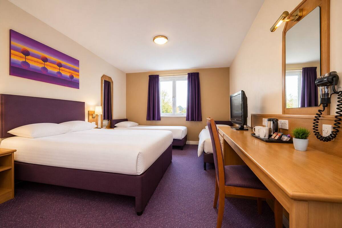 A hotel room with a bed, two bedside tables, a desk with a chair, a television, a coffee maker, and a window with curtains.