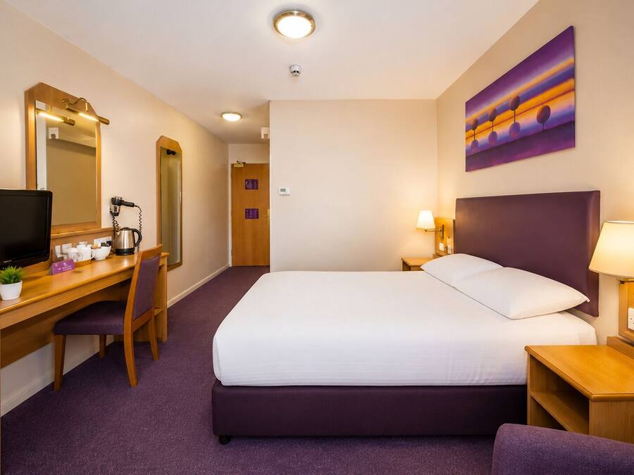 A hotel room with a bed, desk, chair, TV, and a painting on the wall.