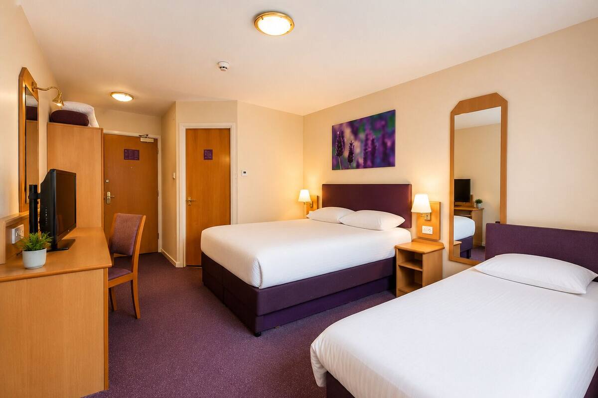 A hotel room with two beds, a desk with a computer, a chair, and a painting on the wall.