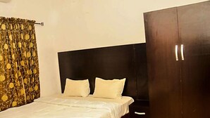 A bedroom with a bed, two pillows, a dark wardrobe, and a curtain with a floral pattern. - D'ISLAND hotel (Lekki)
