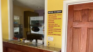 A hotel reception area with a notice to guests detailing check-in time, payment requirements, and amenities like free WiFi and local calls. - The Village Inn (Denham Springs)