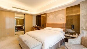 A modern hotel room with a large bed, a seating area, and a bathroom visible through an open door. - Li Cai Tian Qi Hotel Xianyang (Xianyang)