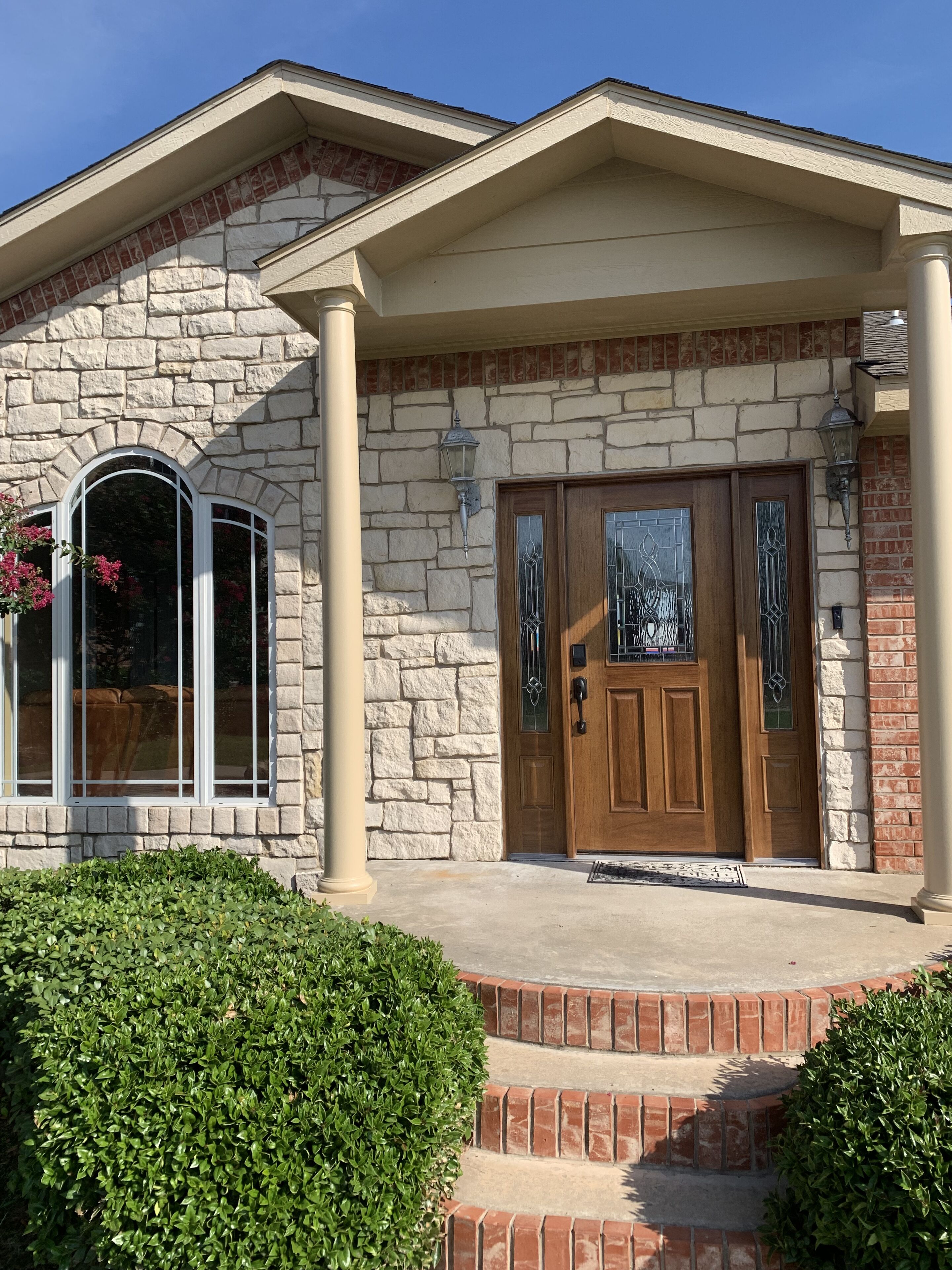 A two-story house with a stone facade, a wooden front door with glass panels, and a small front porch with steps.