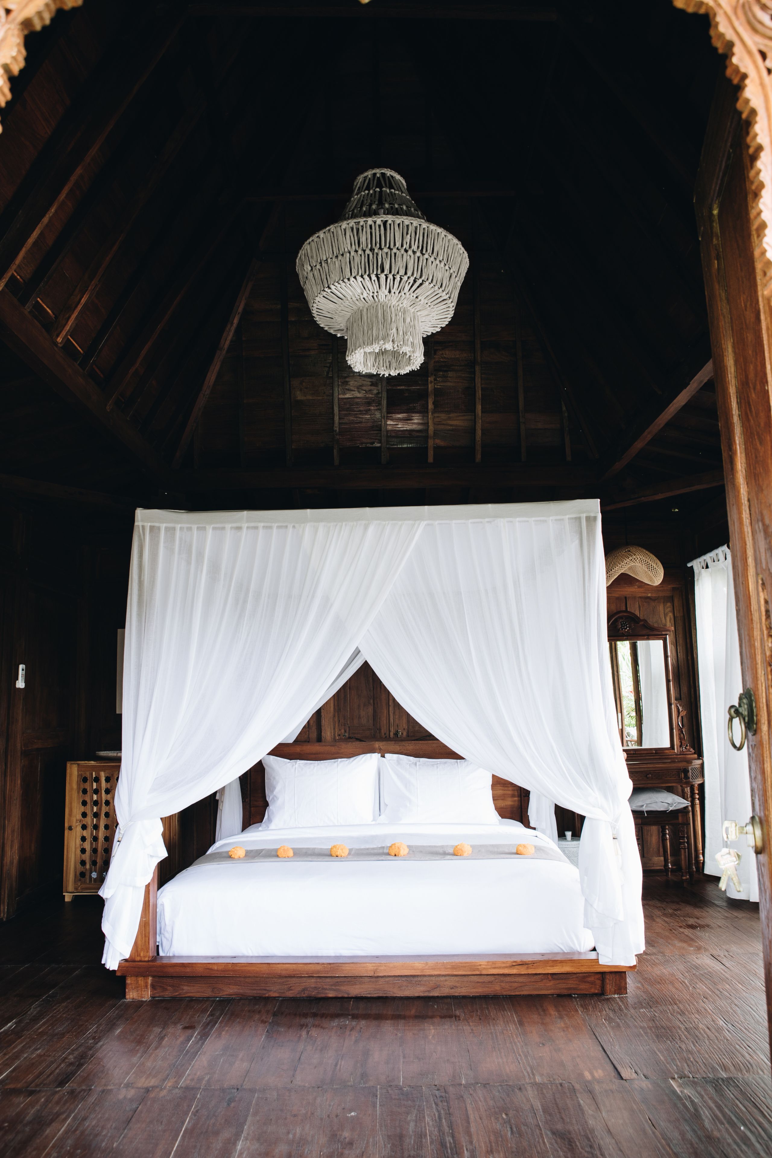 A wooden four-poster bed with white bedding and a canopy, a chandelier, and wooden walls and floors.