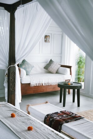 A bedroom with a canopy bed, a small round table, and a view of greenery outside. - White Tortoise Eco Villa's (Pecatu)