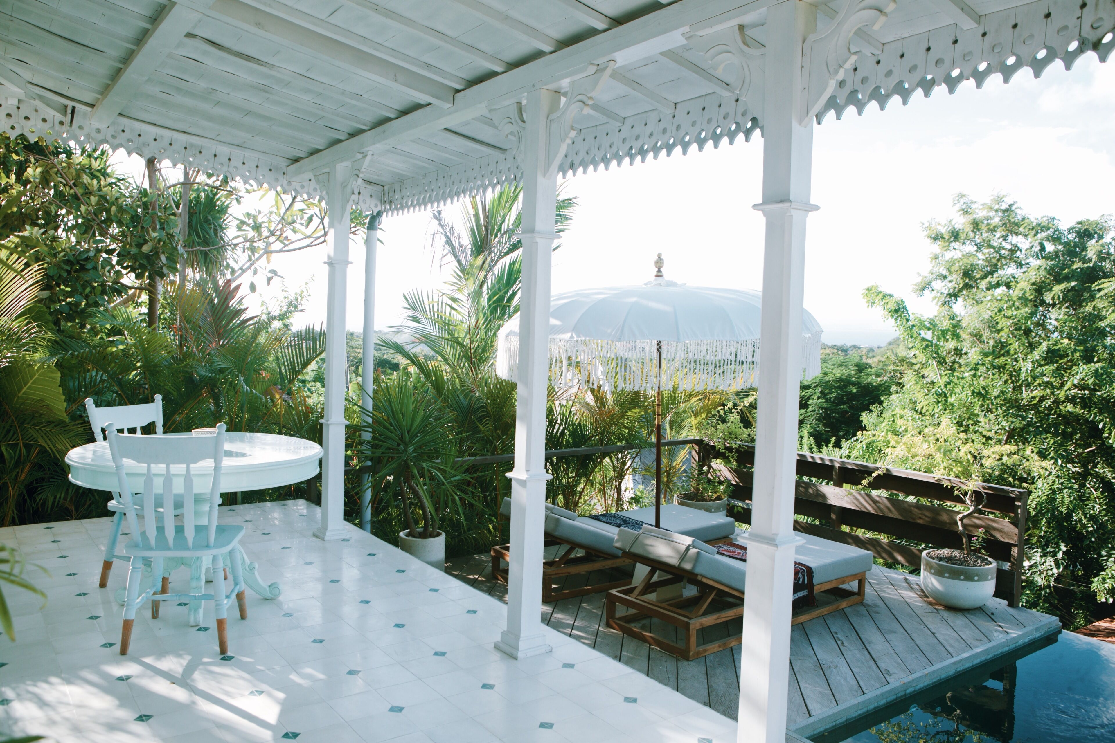 A covered outdoor area with a white gazebo, a round table with chairs, and lounge seating.