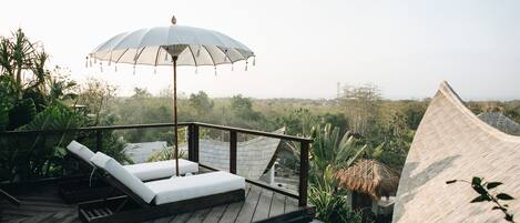 A wooden deck with a white umbrella, a lounge chair, and a view of a lush landscape.