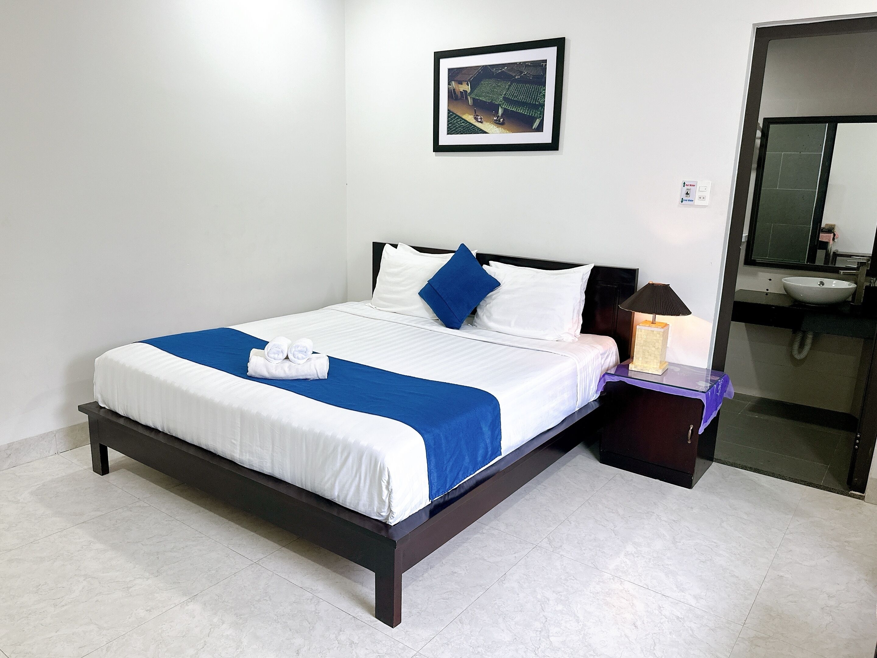 A neatly made bed with white and blue bedding, a dark wooden headboard, and a small bedside table with a lamp and a box.