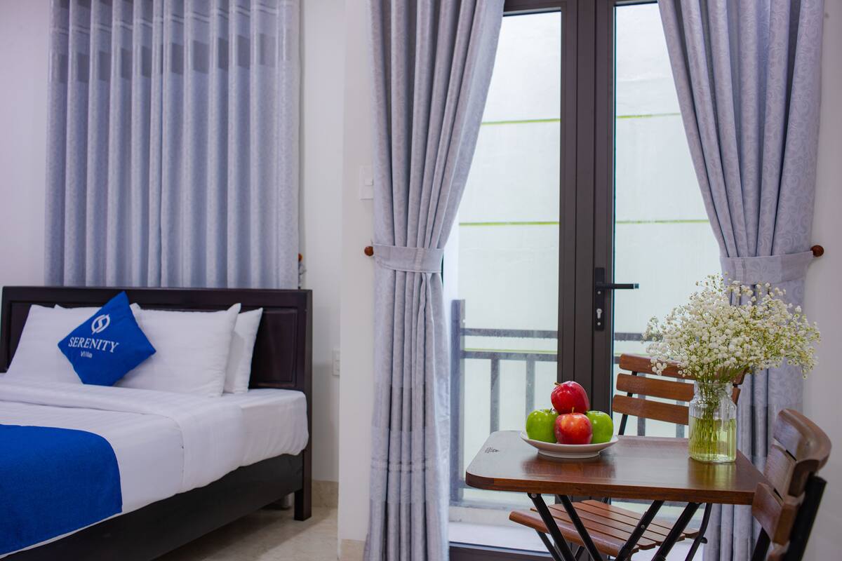 Une chambre d’hôtel avec un lit, une table ornée d’un vase de fleurs et une vue par la fenêtre.