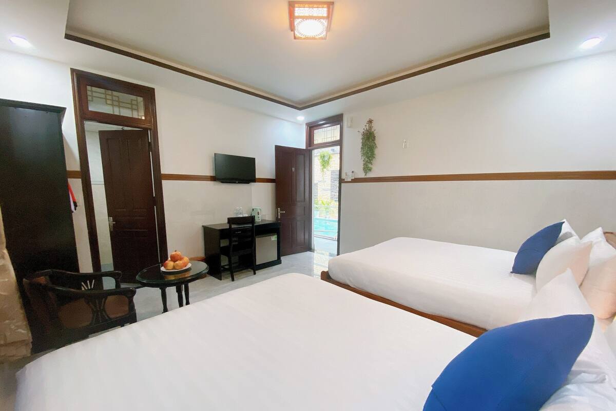 Une chambre d’hôtel avec deux lits, un bureau, une chaise, une petite table avec des fruits et un téléviseur fixé au mur.