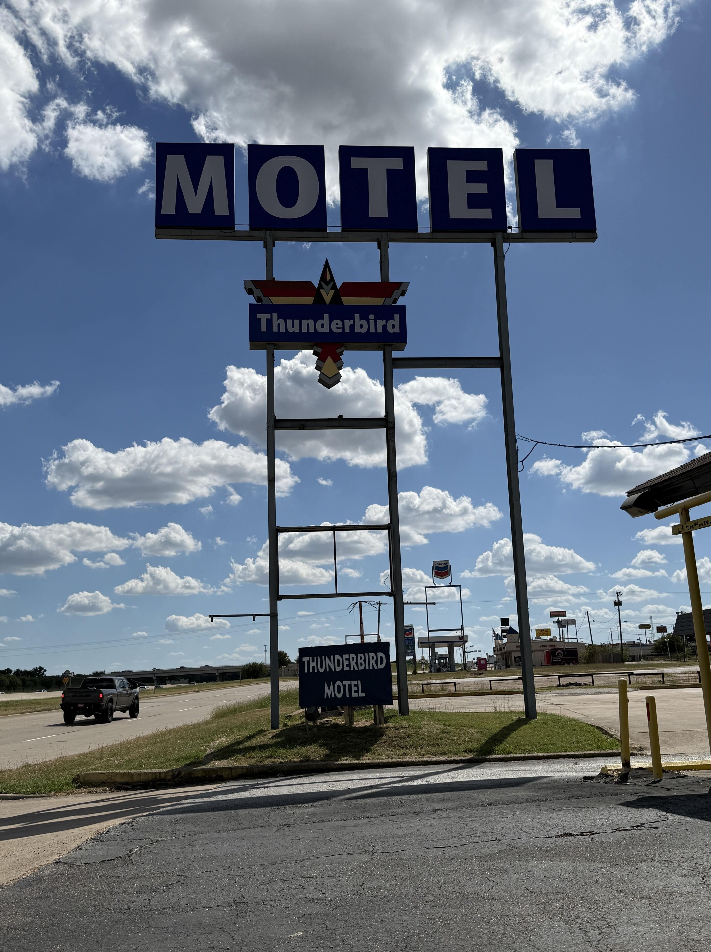 Letrero de motel con la marca 'Thunderbird', cielo despejado y una carretera con vehículos.