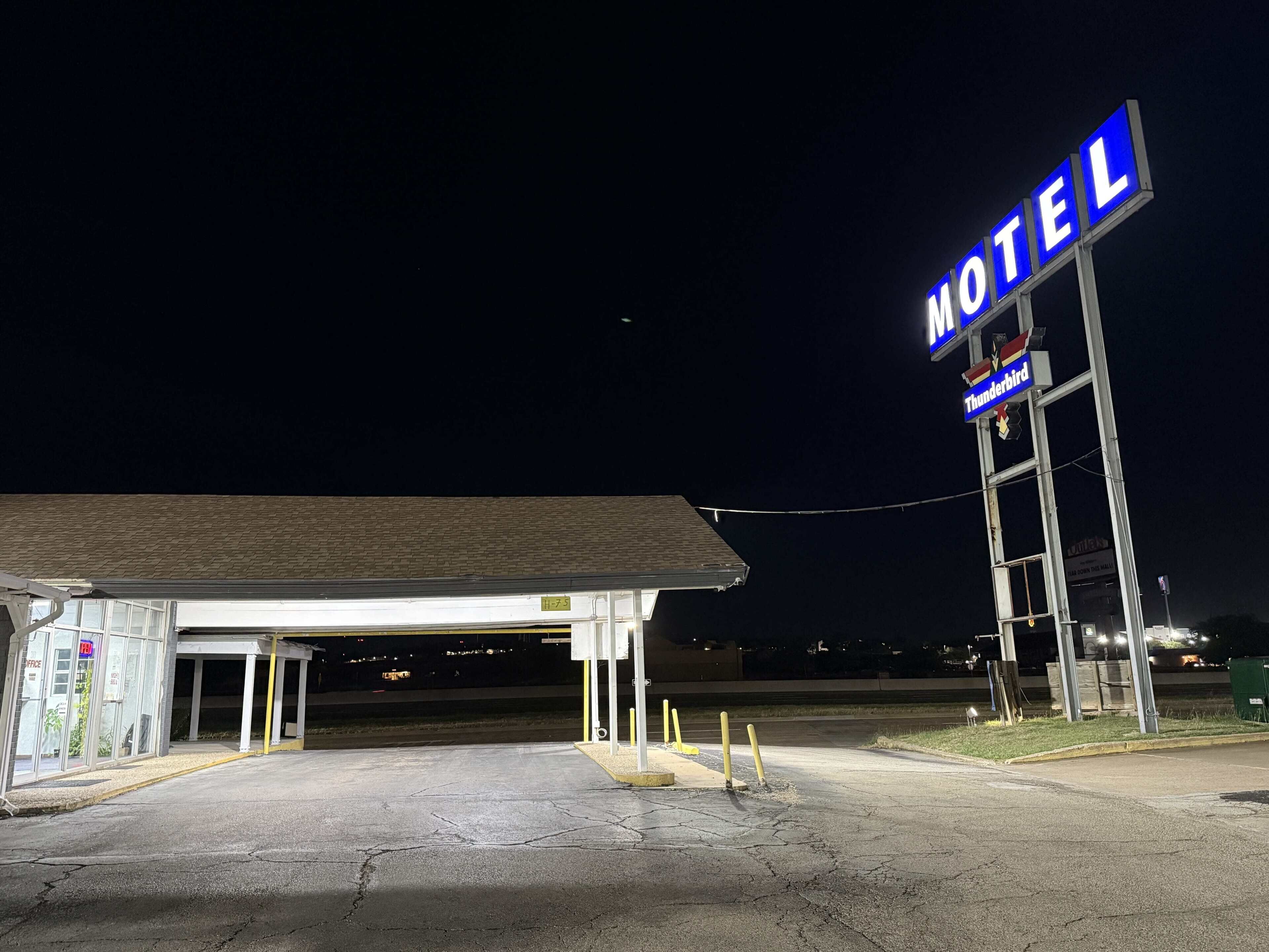 Un motel con un letrero llamativo que dice 'Motel', una zona de estacionamiento techada y una entrada visible.