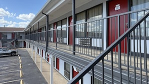 A motel with a row of rooms, each with a red door and a window. There is a parking lot with a car parked in front.