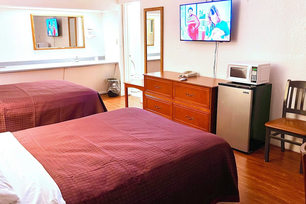 A hotel room with two beds, a dresser, a microwave, a chair, and a television mounted on the wall.