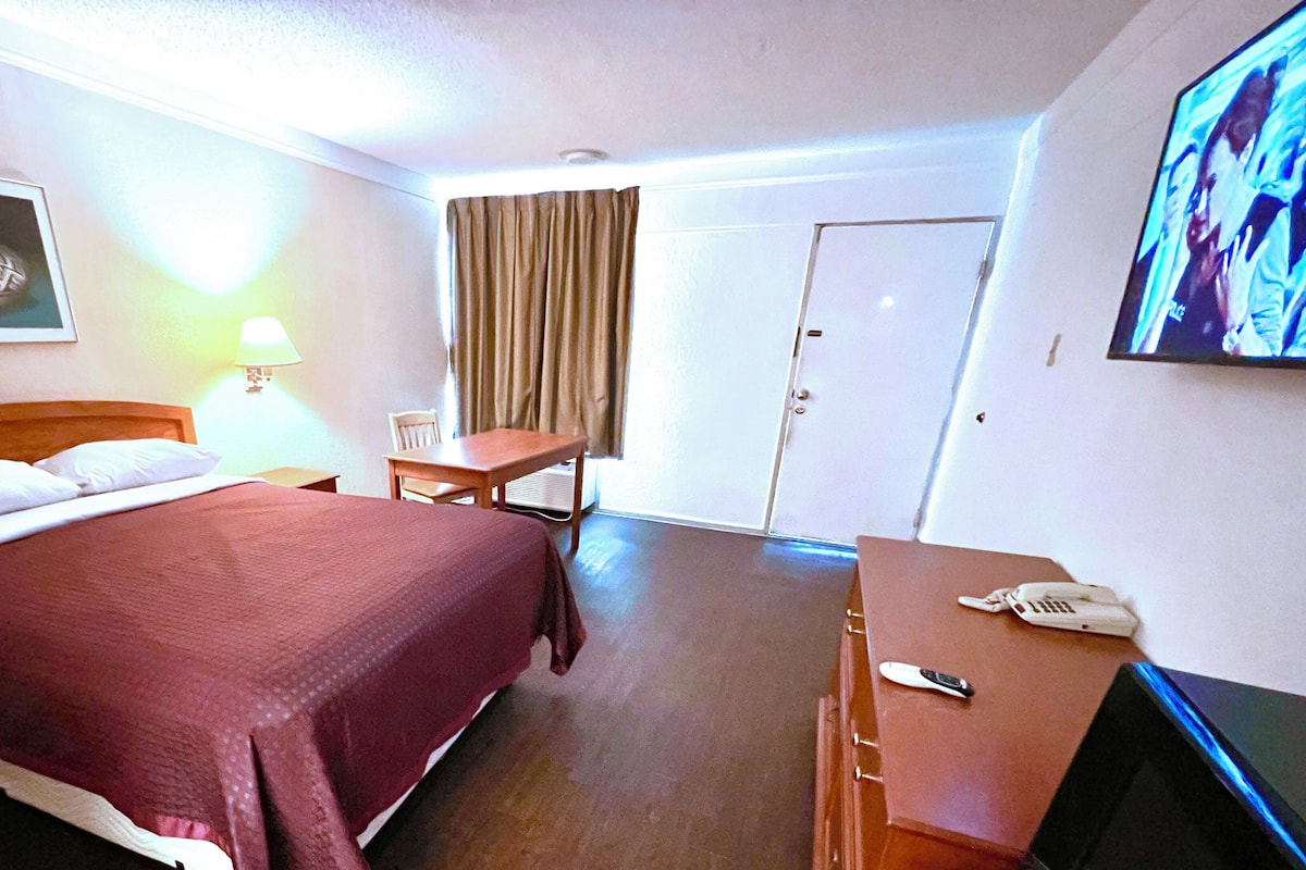 A hotel room with a bed, a desk, a chair, a television, and a door.