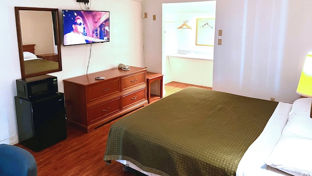 A hotel room with a bed, a dresser, a television, a microwave, and a mirror.