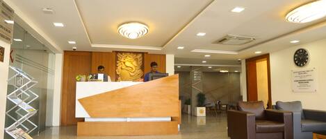 A reception area with a wooden reception desk, a clock on the wall, and a seating area with a sofa and armchairs.