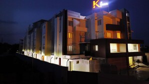 A modern hotel with a prominent 'K' sign, multiple balconies, and a well-lit facade. - Kfour Apartment & Hotels Private Limited (Madurai)