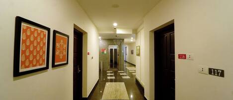 A hotel hallway with framed artwork on the walls, a tiled floor, and numbered doors.