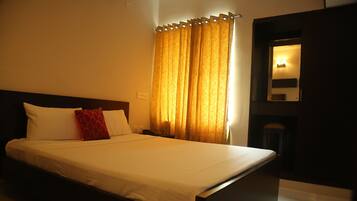 A neatly made bed with white linens and a single red pillow, a wooden headboard, and a window with golden curtains.