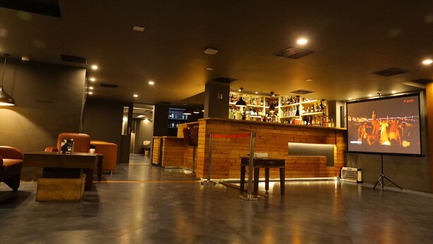 A bar area with a counter, seating, and a projection screen displaying a cityscape. - Kfour Apartment & Hotels Private Limited (Madurai)