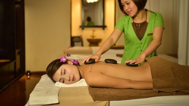 A massage therapy session in a room with a wooden floor, a mirror, and a chandelier.
