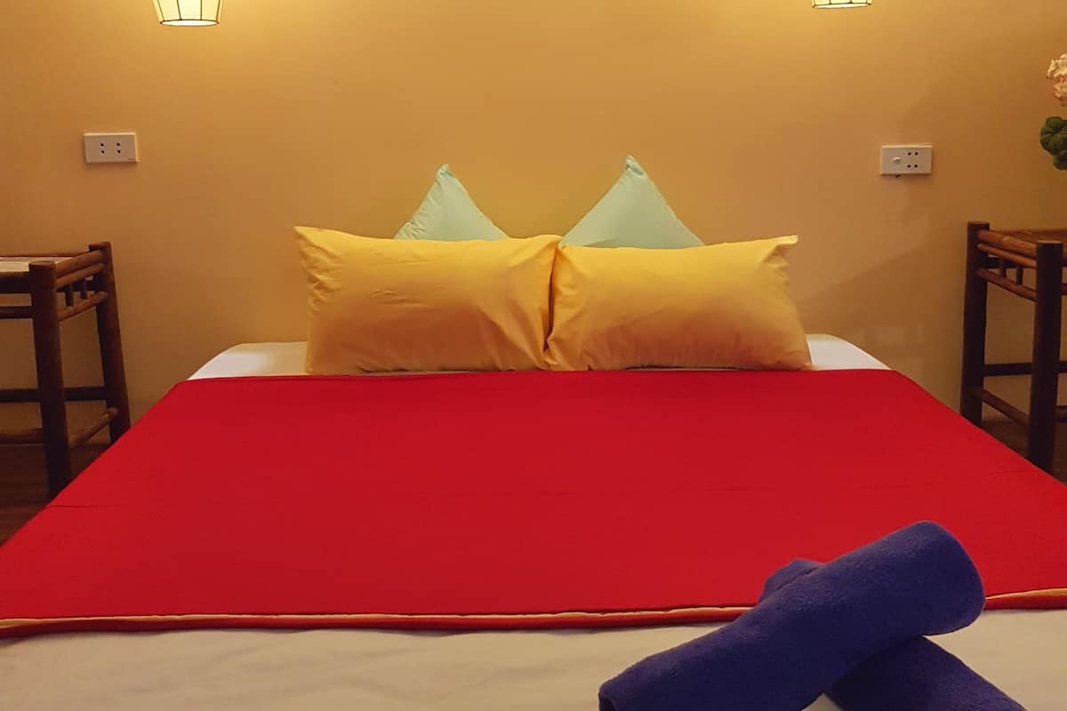 Ein Hotelzimmer mit einem Bett, zwei Nachttischlampen, einer roten Bettdecke und zwei zusammengerollten Handtüchern.