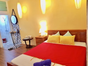 A hotel room with a wooden bed, a red bedspread, and a nightstand with a lamp.
