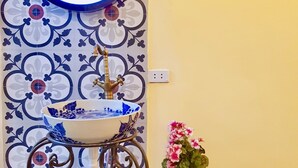 A bathroom with a decorative tile backsplash, a sink with a blue floral pattern, a mirror with a blue frame, and a potted plant with pink flowers.